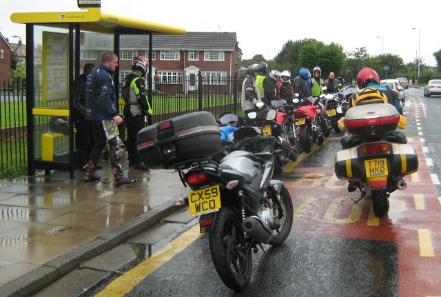 motorcycles and riders in the rain at a bus stop